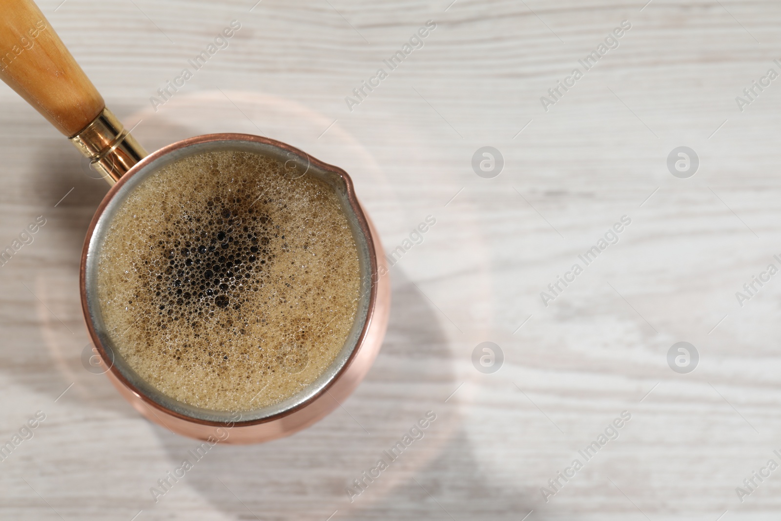 Photo of Cezve with hot aromatic Turkish coffee on white wooden table, top view. Space for text