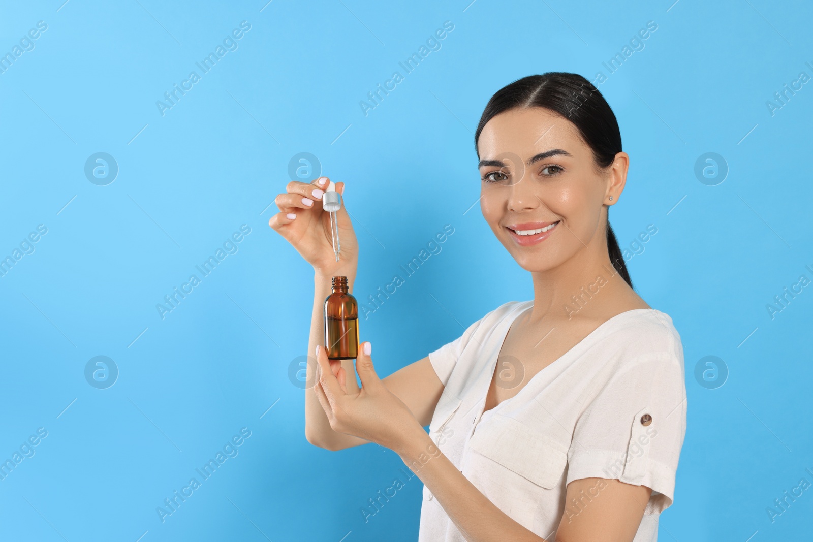 Photo of Young woman with bottle of essential oil on light blue background. Space for text
