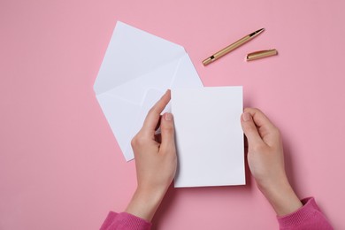 Woman with blank card at pink table, top view. Space for text