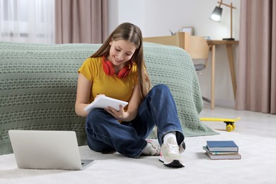 Photo of Online learning. Teenage girl writing in notepad near laptop at home