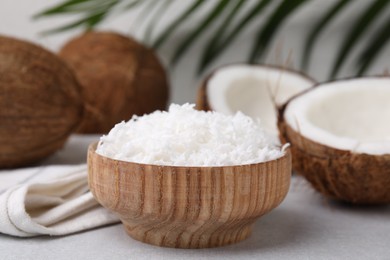 Coconut flakes in bowl and nuts on light grey table