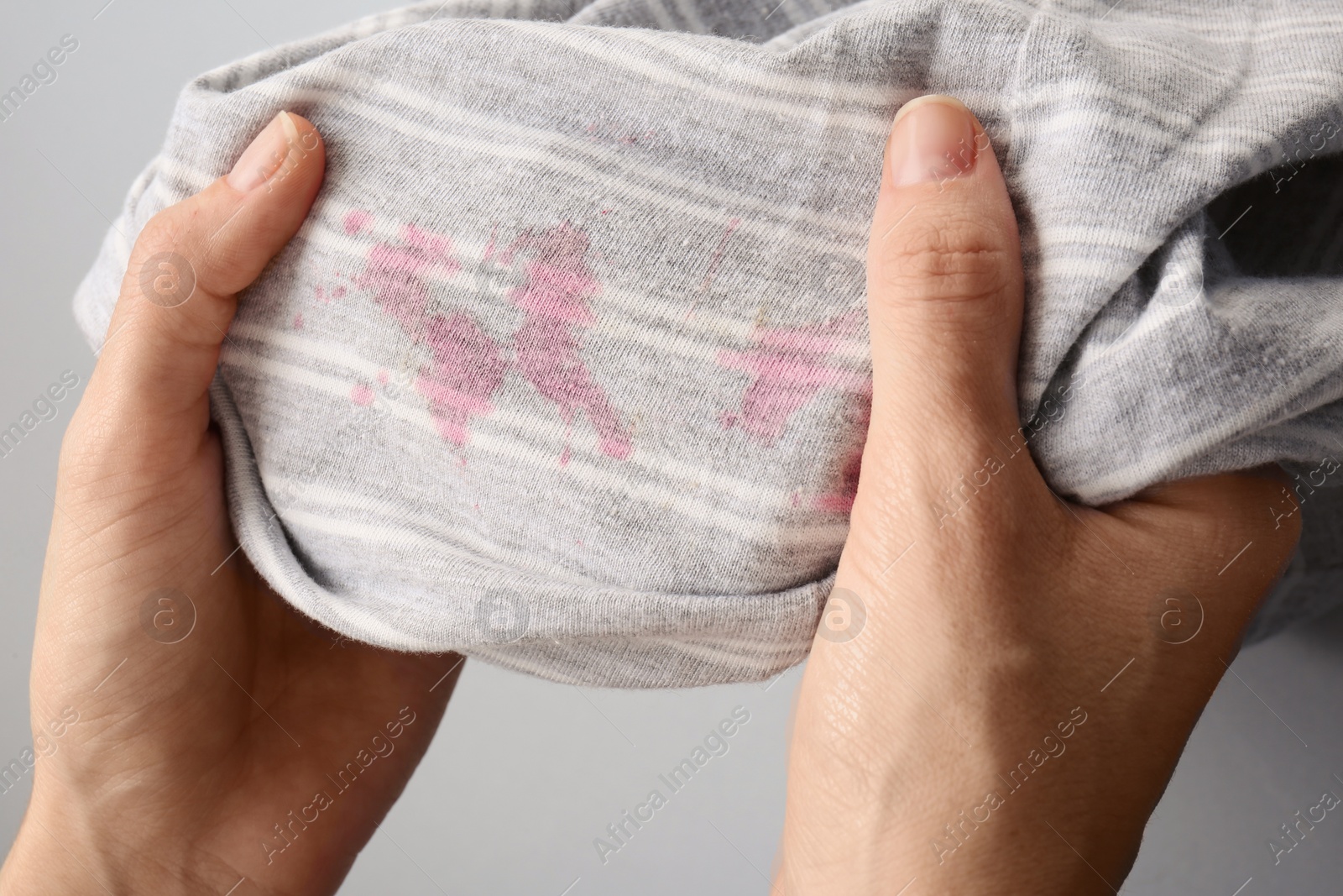 Photo of Woman holding striped shirt with stains on light grey background, closeup