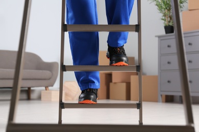 Photo of Professional worker climbing up ladder in room, closeup