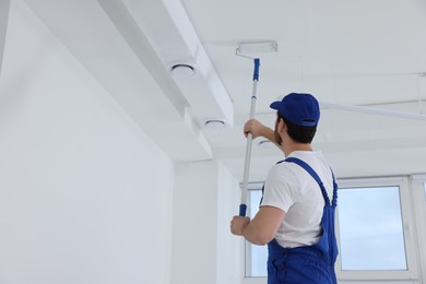 Photo of Handyman painting ceiling with roller in room, back view