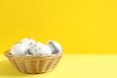 Photo of Wicker bowl of Easter eggs on table against color background. Space for text