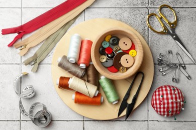 Photo of Flat lay composition with spools of threads and sewing tools on light tiles