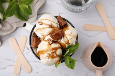 Photo of Scoopsice cream with caramel sauce, candies and mint leaves on white textured table, flat lay