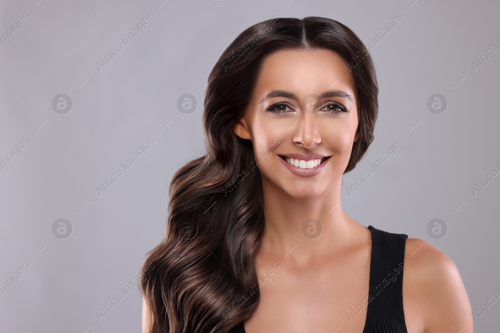 Image of Gorgeous woman with shiny wavy hair on grey background. Professional hairstyling