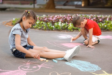 Little children drawing with colorful chalk on asphalt