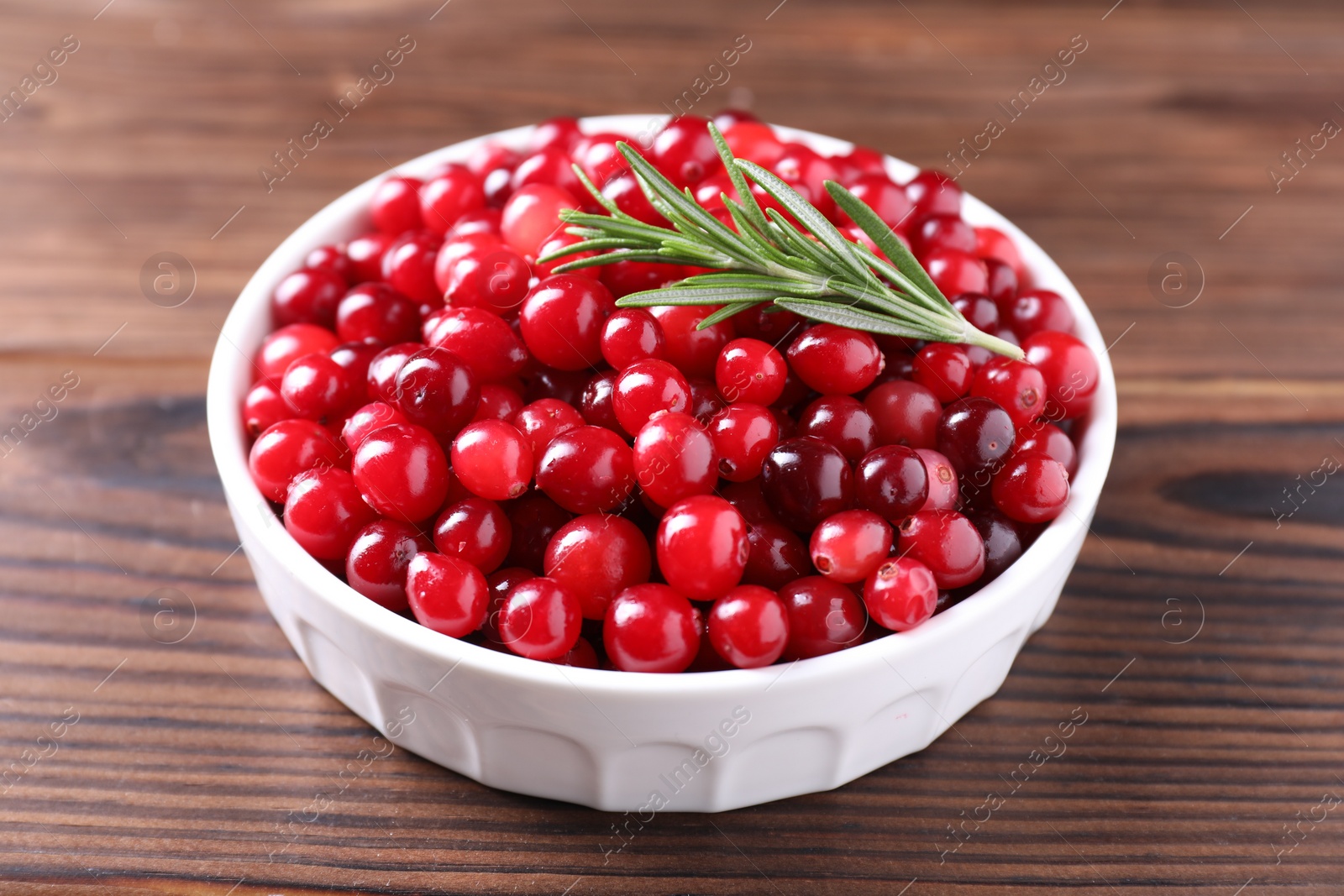 Photo of Fresh ripe cranberries and rosemary in bowl on wooden table, closeup