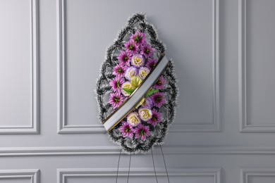 Funeral wreath of plastic flowers with ribbon near light grey wall