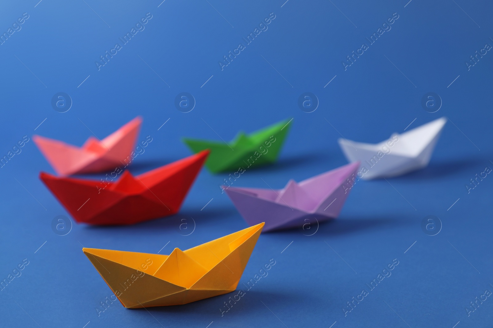 Photo of Many colorful handmade paper boats on blue background. Origami art