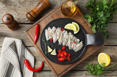 Tasty anchovies with spices and products on wooden table, flat lay