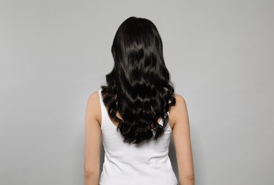 Photo of Young woman with long curly hair on grey background, back view