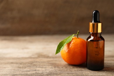 Bottle of tangerine essential oil and fresh fruit on wooden table, closeup. Space for text