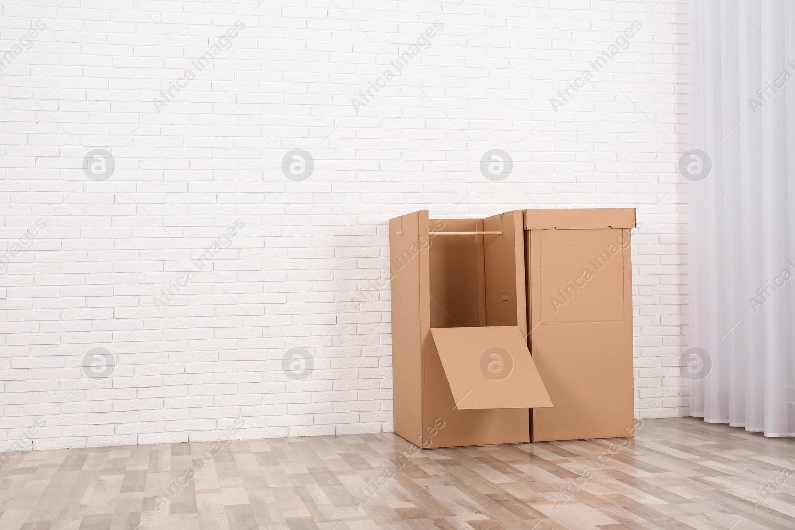 Photo of Empty cardboard wardrobe boxes against brick wall indoors. Space for text