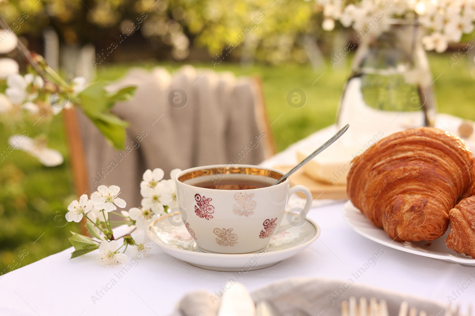 Photo of Stylish table setting with beautiful spring flowers, tea and croissants in garden