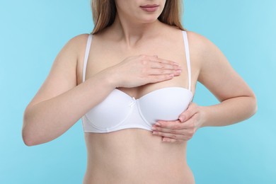 Photo of Mammology. Young woman doing breast self-examination on light blue background, closeup