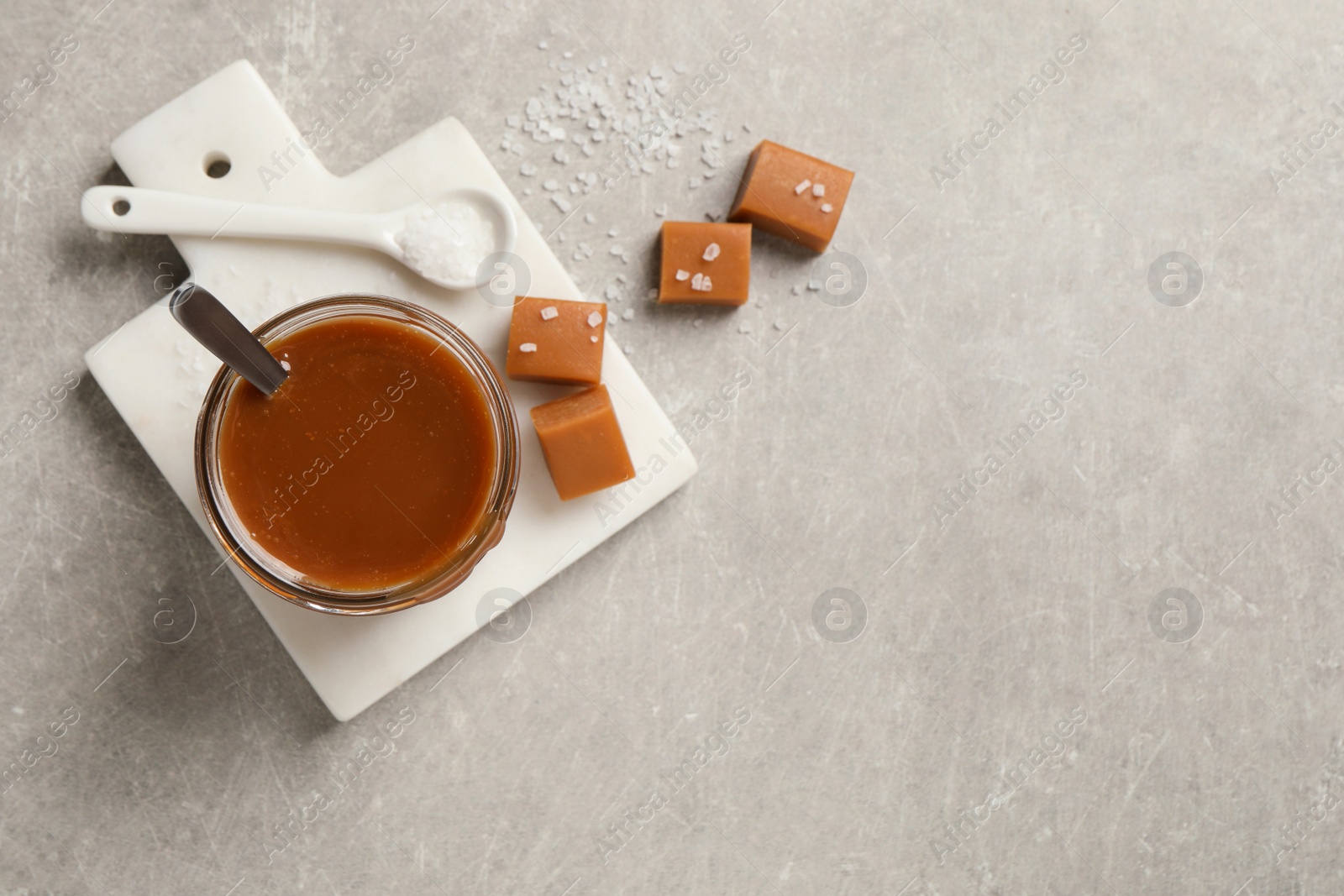 Photo of Tasty salted caramel and candies on light grey table, flat lay. Space for text