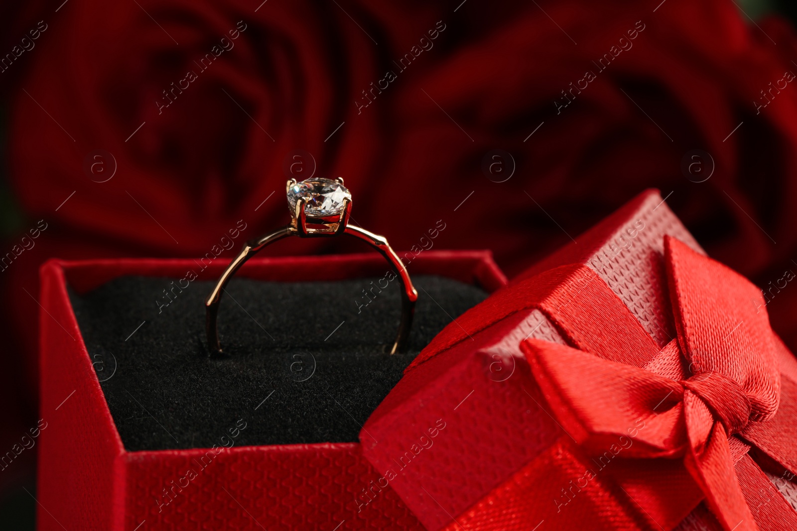 Photo of Beautiful engagement ring with gemstone in box against roses, closeup