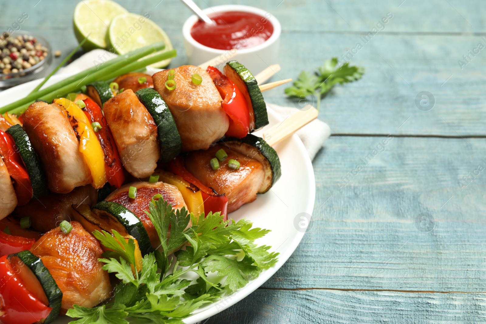 Photo of Delicious chicken shish kebabs with vegetables and parsley on light blue wooden table, closeup. Space for text