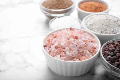 Different kinds of salt on white marble table, space for text