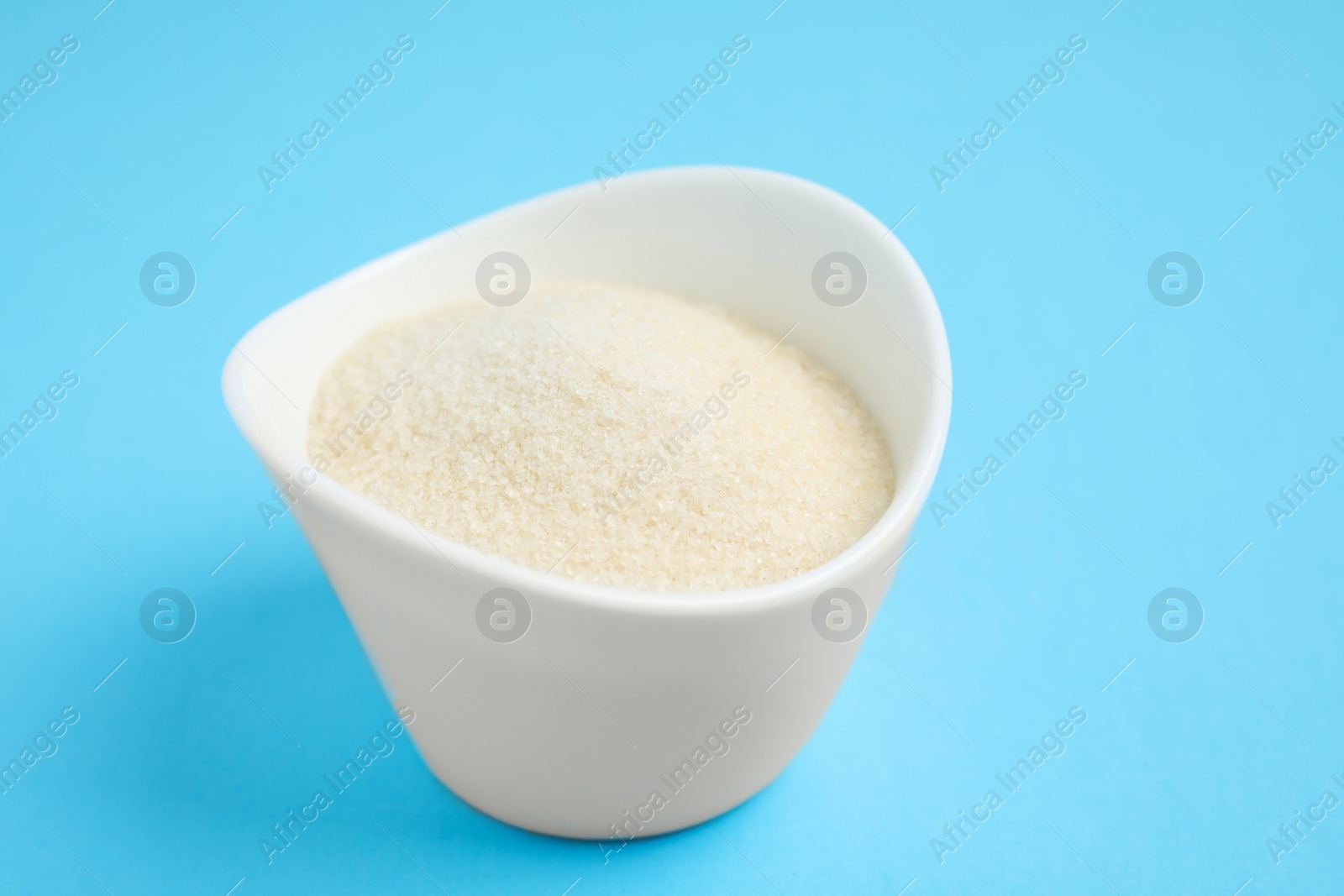 Photo of Gelatin powder in bowl on light blue background, closeup