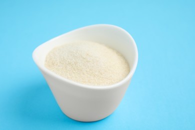 Photo of Gelatin powder in bowl on light blue background, closeup