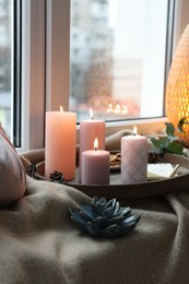 Tray with burning wax candles and decor on window sill indoors