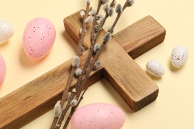 Photo of Wooden cross, painted Easter eggs and willow branches on beige background, closeup