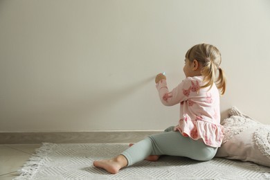 Photo of Little girl drawing on beige wall indoors, space for text. Child`s art