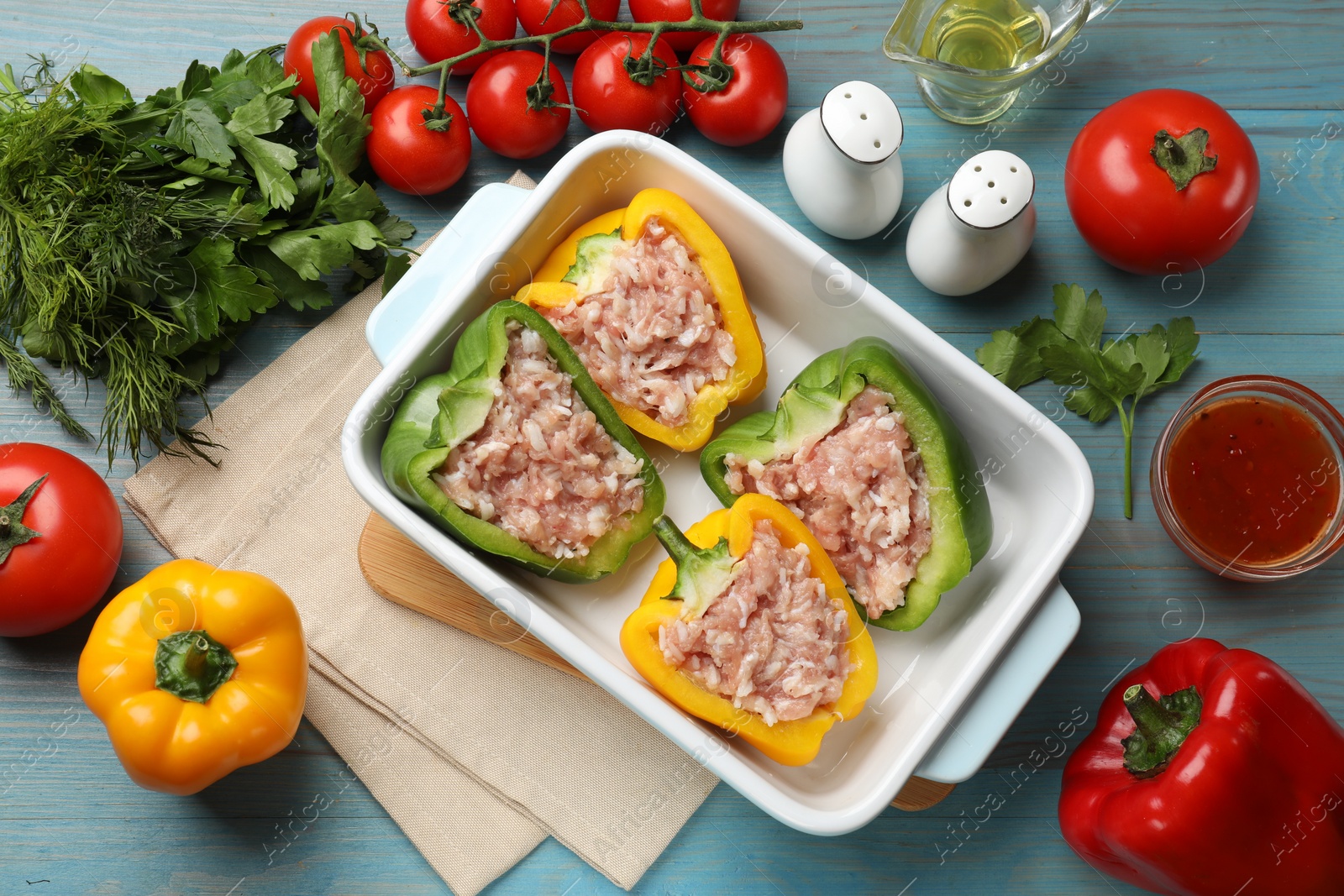 Photo of Raw stuffed peppers in dish and ingredients on wooden table, flat lay