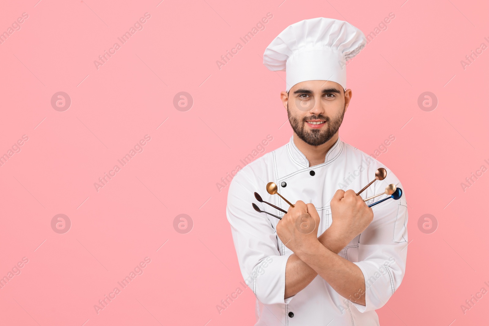 Photo of Professional chef holding kitchen utensils on pink background. Space for text