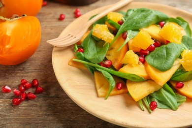 Photo of Delicious persimmon salad with pomegranate and spinach on wooden table, closeup