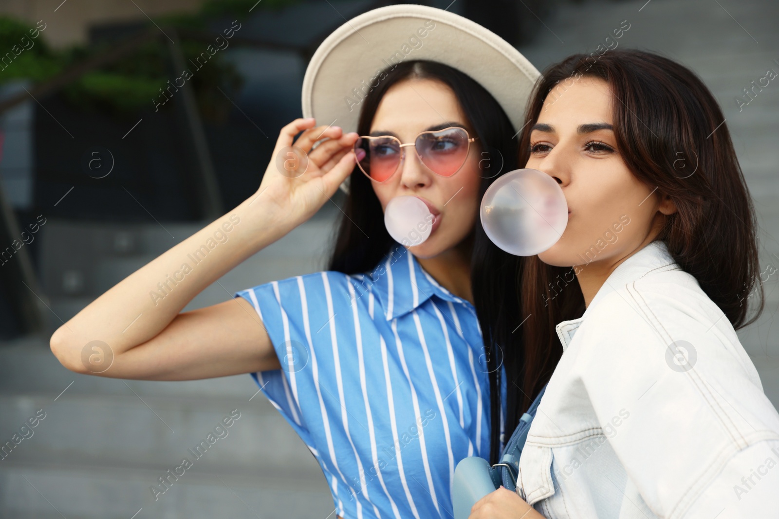 Photo of Beautiful stylish women blowing gums near stairs outdoors