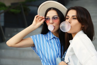 Beautiful stylish women blowing gums near stairs outdoors
