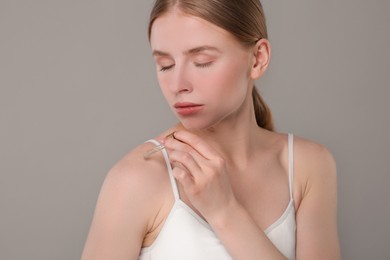 Photo of Beautiful young woman applying essential oil onto shoulder on grey background