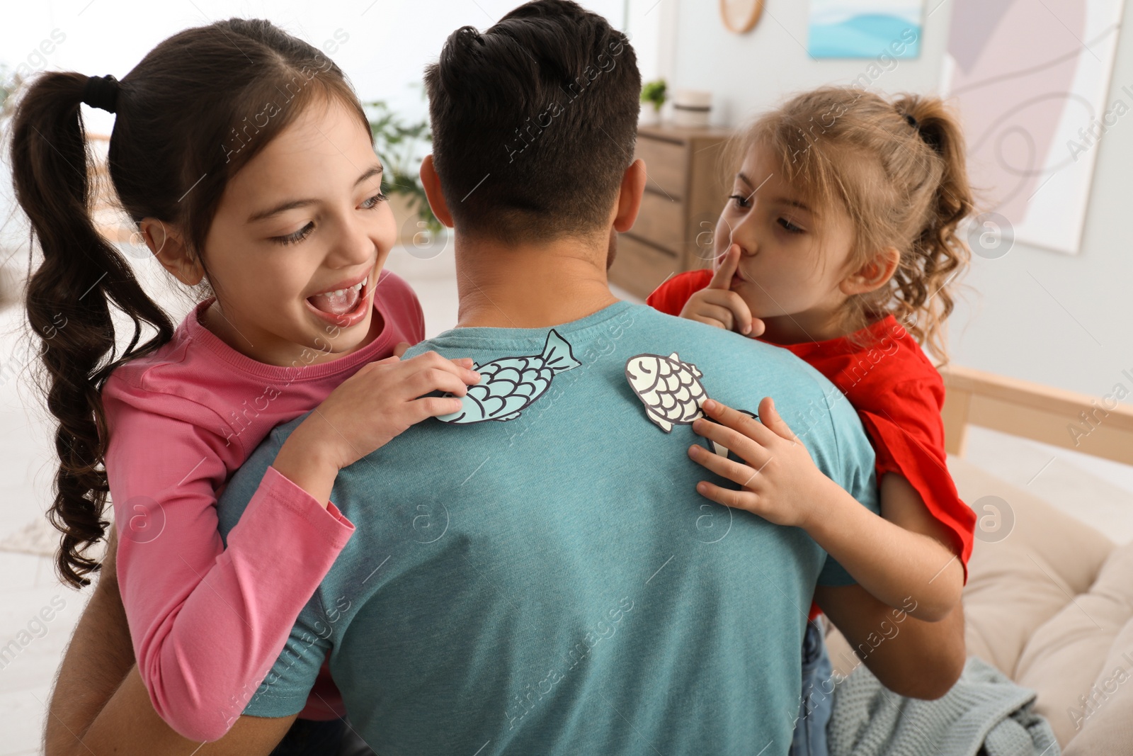 Photo of Cute little children sticking paper fish to father's back at home