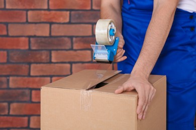 Photo of Worker taping box with adhesive tape dispenser near brick wall, closeup