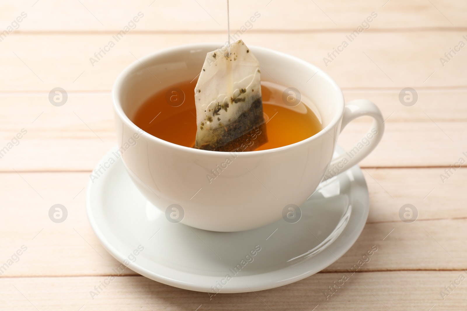Photo of Putting tea bag in cup on light wooden table, closeup