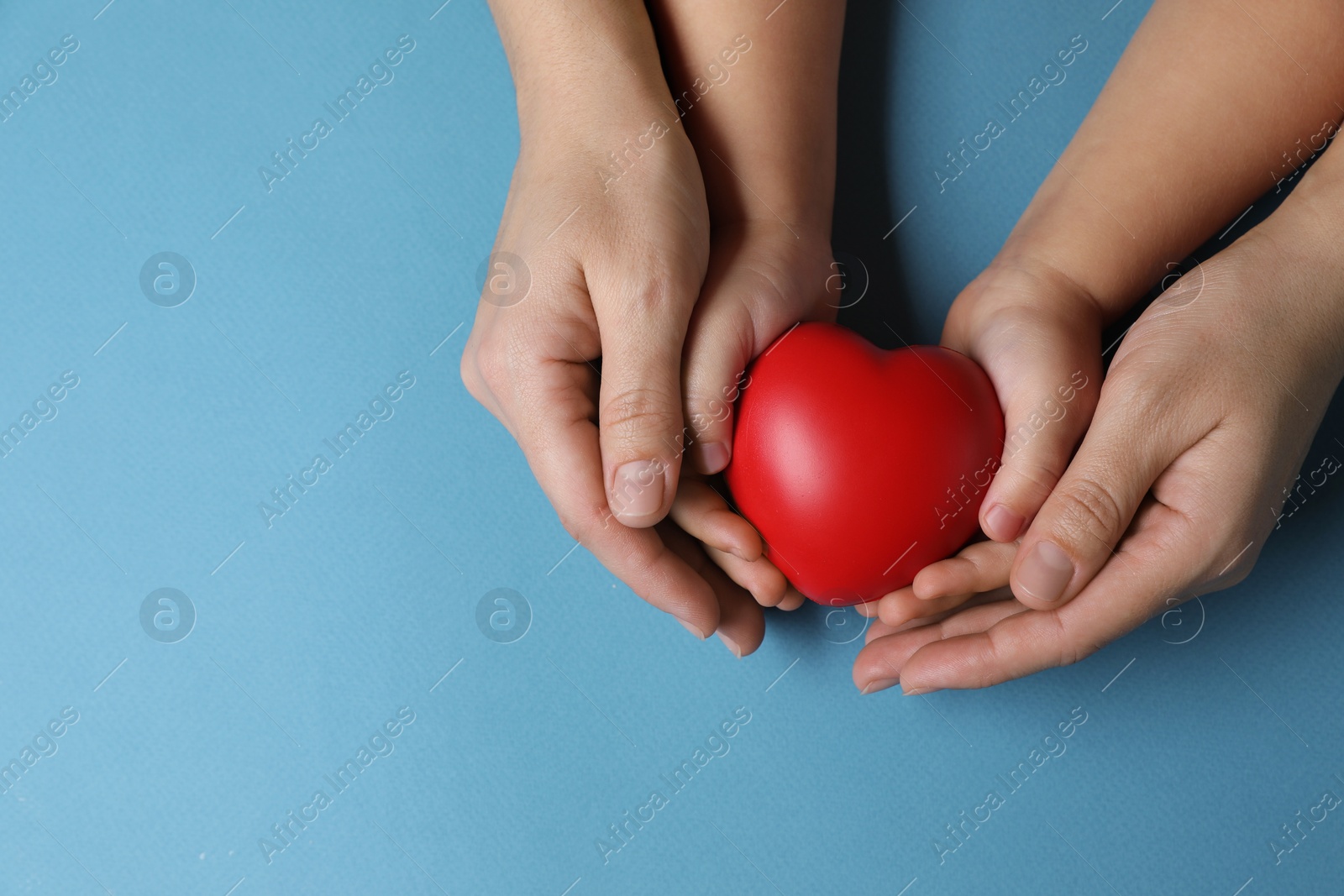 Photo of Mother and her child holding red decorative heart on light blue background, top view. Space for text