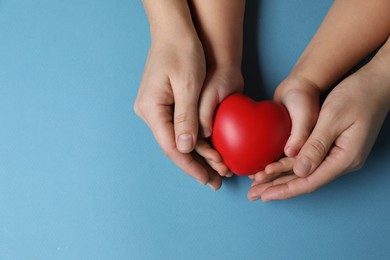 Photo of Mother and her child holding red decorative heart on light blue background, top view. Space for text