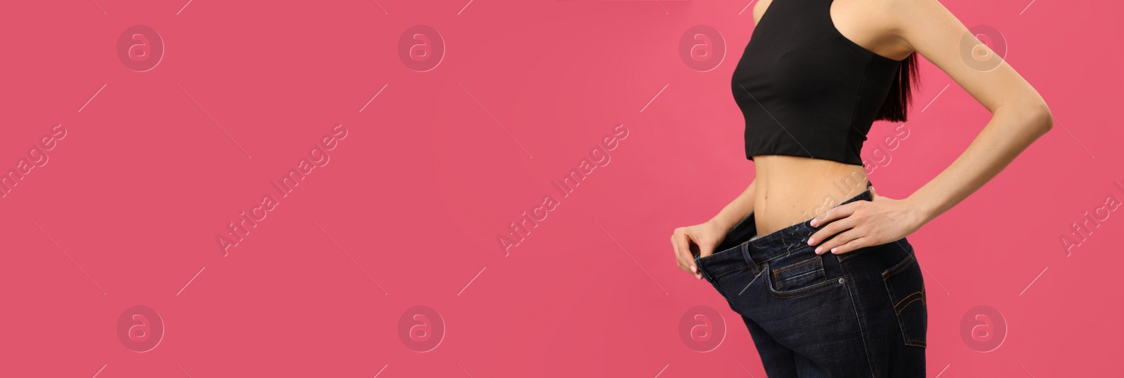 Photo of Young woman wearing big jeans after weight loss on pink background, closeup