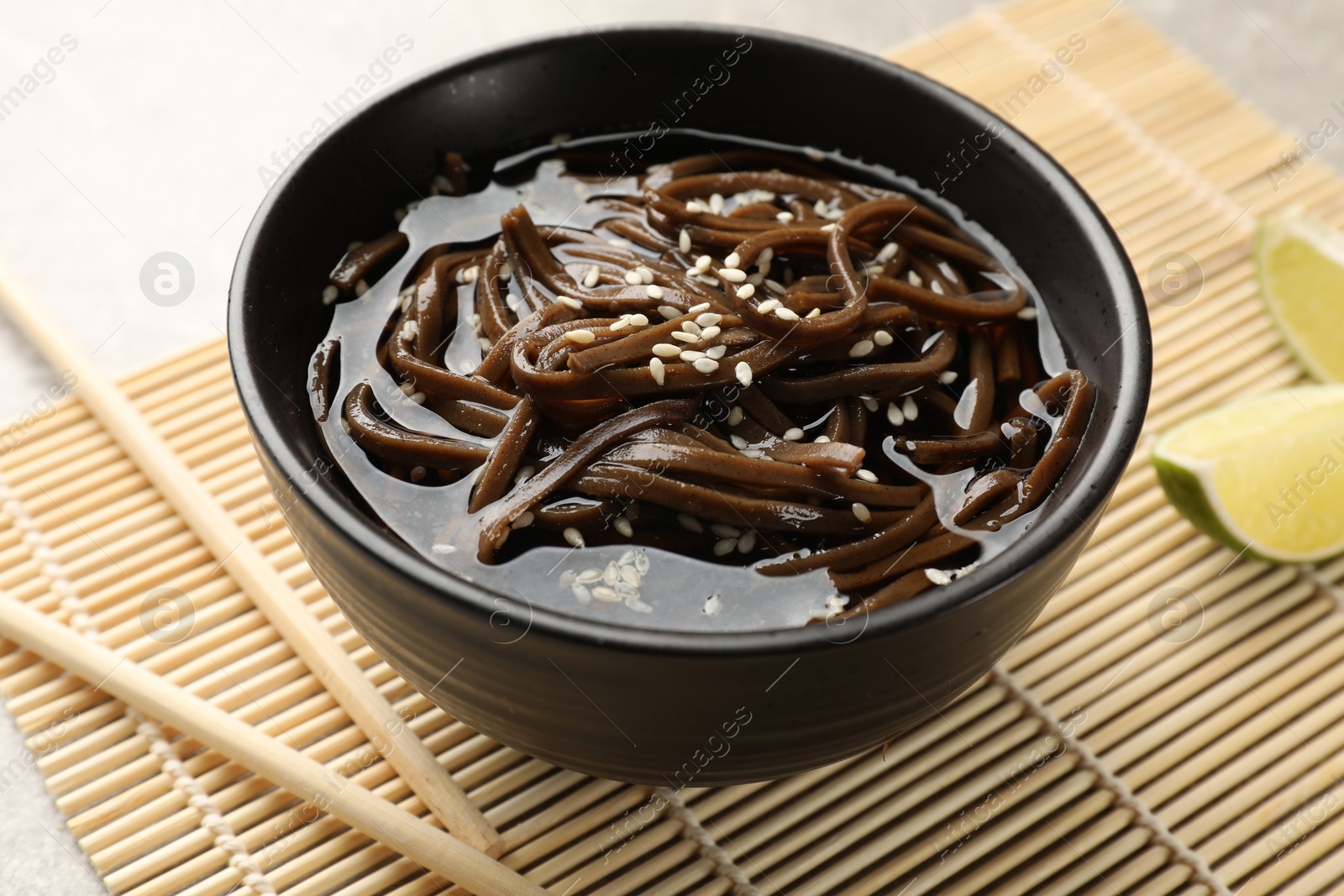 Photo of Tasty buckwheat noodles (soba) with sauce in bowl and chopsticks on table, closeup