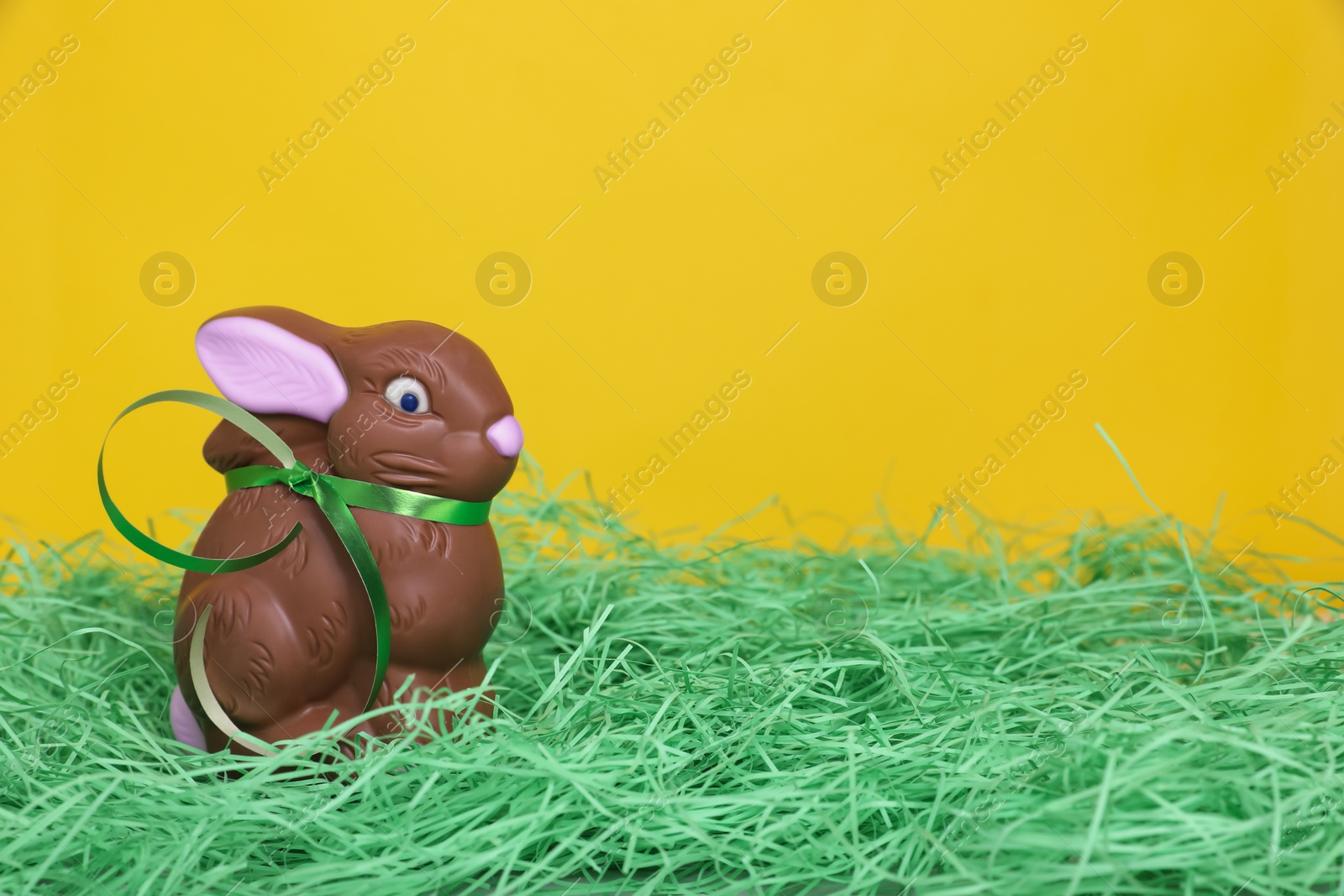 Photo of Easter celebration. Cute chocolate bunny on grass against yellow background, space for text