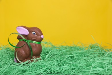 Photo of Easter celebration. Cute chocolate bunny on grass against yellow background, space for text