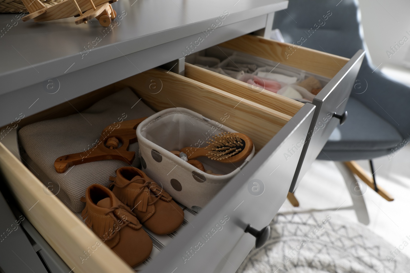 Photo of Open cabinet drawer with baby shoes and accessories in child room