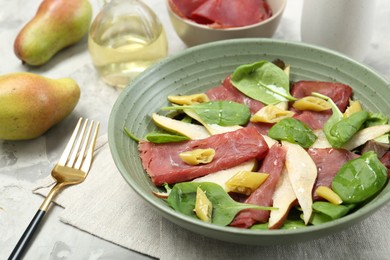 Photo of Delicious bresaola salad in bowl, fork and ingredients on light table, closeup