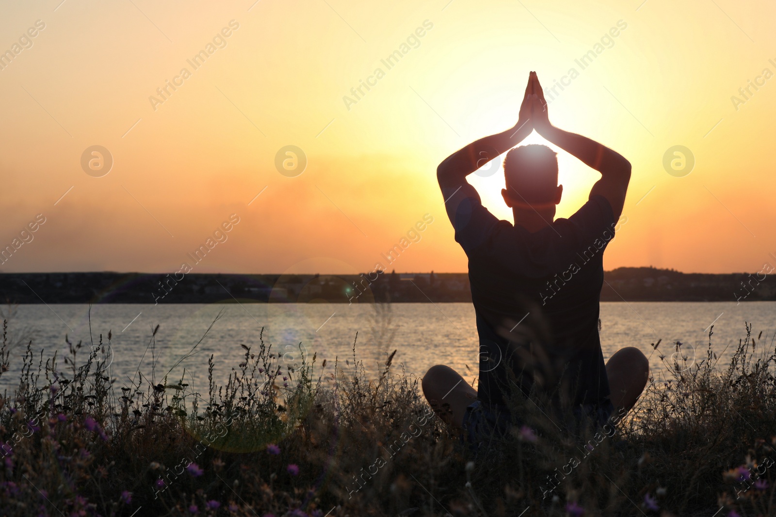 Photo of Man meditating near river at sunset, back view. Space for text