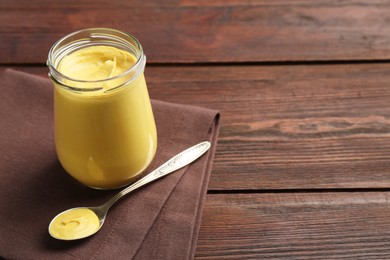 Photo of Glass jar and spoon with tasty mustard sauce on wooden table, space for text